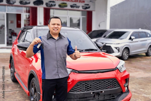 Fototapeta Young handsome smiling Asian man holding car keys, getting a new car and showing thumbs up. Buy or rent a car concept