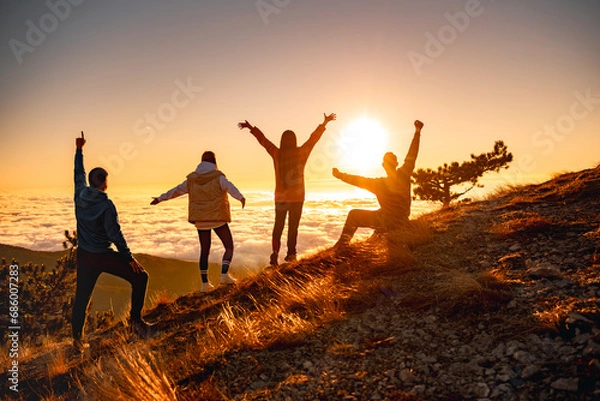 Obraz Group of happy friends are standing at mountain top and greeting sunrise or sunset above clouds