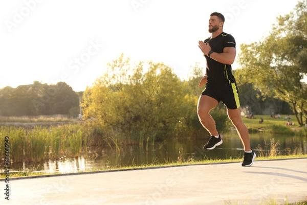 Fototapeta Young man running near pond in park. Space for text