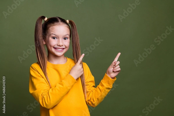 Obraz Photo of positive schoolgirl with ponytails wear yellow pullover indicating at sale empty space isolated on khaki color background