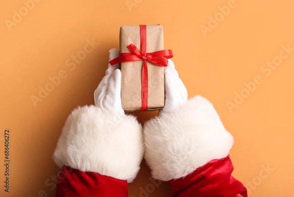 Obraz Santa hands with gift box on color background, closeup