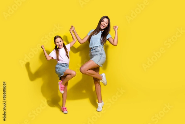 Fototapeta Photo of of two excited sisters raise fists winning school contests isolated over bright color background