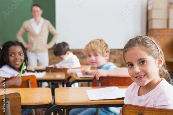 Fototapeta Pupils and teacher smiling at camera in classroom
