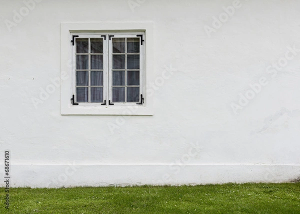 Fototapeta The old white plastered wall with a window and green lawn before