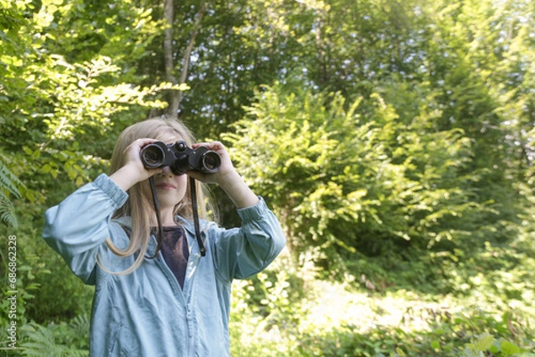 Obraz Cute little girl exploring nature looking through binoculars. Child playing outdoors. Kids travel, adventure and bird watching concept.	