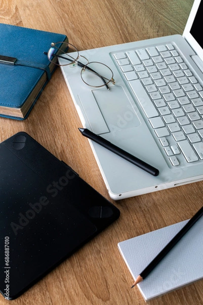 Obraz white laptop on a wooden table with blue agenda and graphic tablet, glasses on a white laptop, work and study space, graphic design