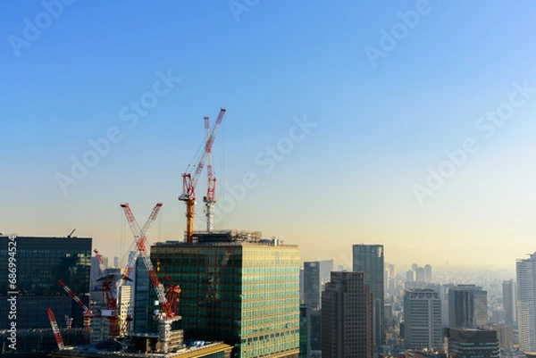 Fototapeta Tower cranes and unfinished buildings, construction cranes on blue sky with city skyscrapers background at construction site.