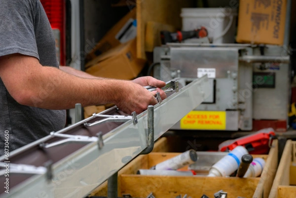 Obraz Hands of a Technician in the process of installing custom-made gutters on our home in Windsor in Upstate NY.  The skilled hands of a craftsman preparing gutters for installation.  
