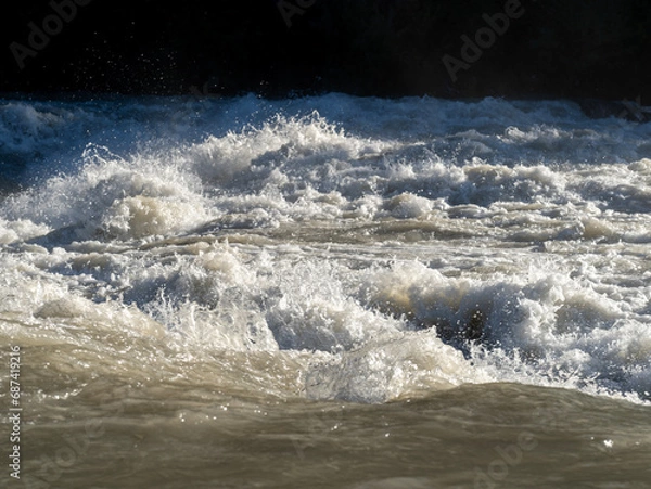 Fototapeta The river swollen after heavy rainfall and floodwater crashing through valley. The water flows fast from the high valley to the plain. General contest of a river in flood