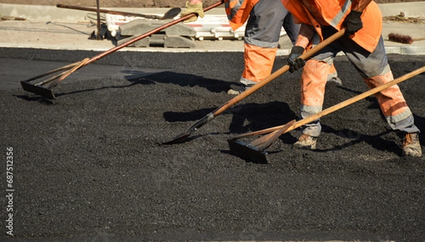 Obraz workers with rakes level the asphalt mixture