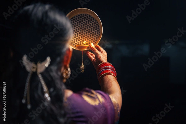 Fototapeta An Indian woman looking at the moon through a sieve during the Karwa Chauth festival.