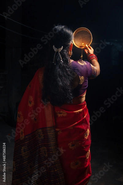 Fototapeta An Indian woman looking at the moon through a sieve during the Karwa Chauth festival.