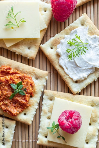 Obraz Close up o Various kind of salty crackers with vegan meat and vegan cream cheese decorated with fresh herbs and raspberries. Vegan food concept.