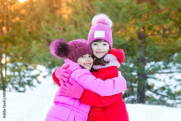 Fototapeta Two little girls in a snowy forest. Two sisters hugging and smiling, looking at the camera. Happy girls hugging. Winter. Place for text. Sisters day