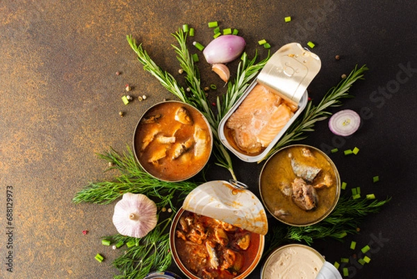 Fototapeta Different open tin cans with canned fish among spices and herbs on a brown background, canned salmon and mackerel, sprat and sardine, tuna and herring and fish pate, top view