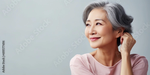 Obraz Happy Asian Woman. Portrait of Beautiful Older Mid Aged Mature Smiling Woman in Pink Clothes Isolated on Grey Background. Anti-aging Skin Care Face Beauty Product. Banner with Copy Space.