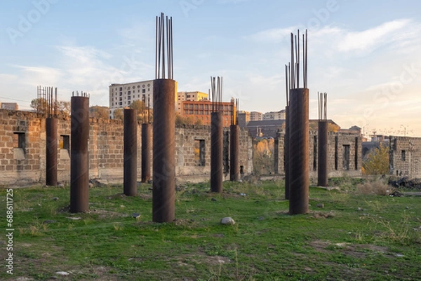 Fototapeta Abandoned construction site. Columns with protruding reinforcement. Construction of house is temporarily frozen. Construction site overgrown with grass. Abandoned walls from unfinished building