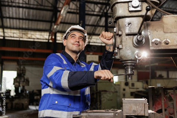 Fototapeta Male workers wearing uniform safety and hardhat working an iron cutting machine in factory. Engineering worker man work machine lathe metal.