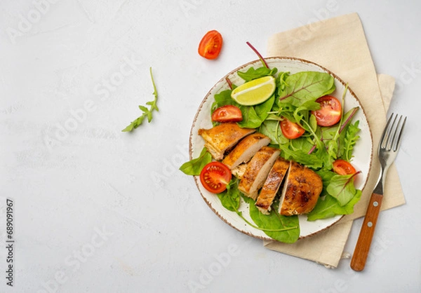 Fototapeta Salad with chicken breast, fillet with lettuce and cherry tomatoes on a plate on a light background, horizontal, free space for copying..