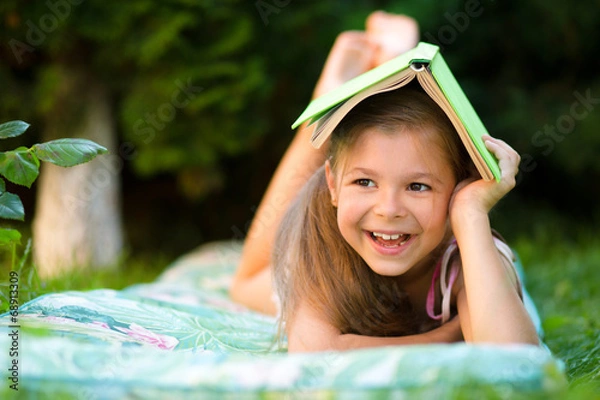 Obraz Little girl is hiding under book outdoors
