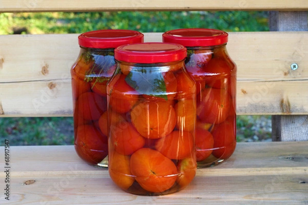 Fototapeta Group of three glass cans of red tomatoes  on the  wooden bench