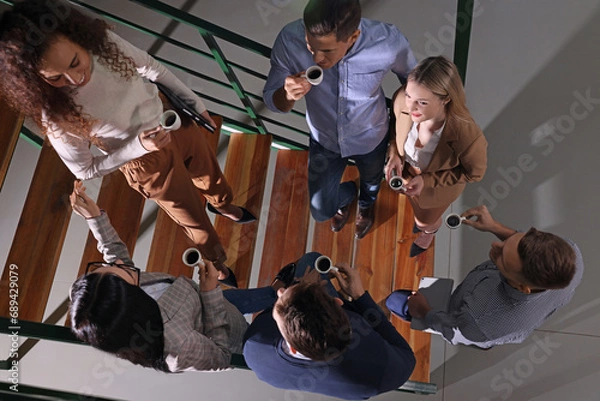 Fototapeta Group of coworkers talking during coffee break on stairs in office, top view