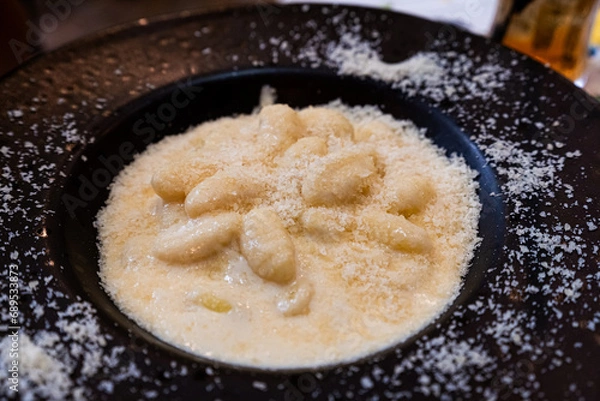 Obraz Classic gnocchi ai 4 formaggi, four cheese pasta, covered with parmesan and served on black plate 