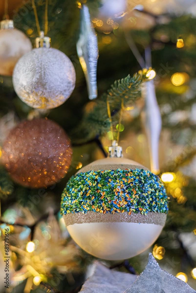 Fototapeta Festive glass balls with colored sparkles, Christmas tree and yellow bokeh of glowing garland.