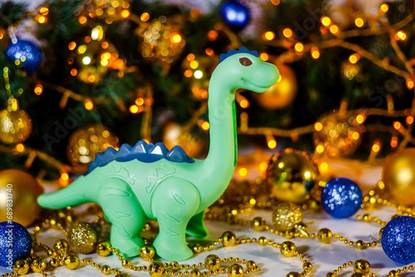 Fototapeta Green dragon on Christmas background. New Year's background of a Christmas tree and a golden garland. Dinosaur. Greeting card. Space for text. Chinese New Year. Christmas, New Year