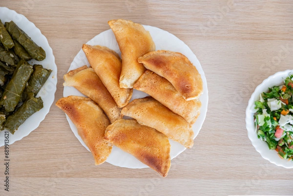 Fototapeta Dish of grape rolls on wooden table from top view with sambousek and qatayef