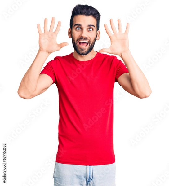 Fototapeta Young handsome man with beard wearing casual t-shirt showing and pointing up with fingers number ten while smiling confident and happy.