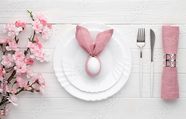 Obraz Easter holiday table setting with egg on plate and cutlery, sakura blossom, pink spring flowers. White wooden background. Top view, flat lay. Lunch or dinner invitation design. Food concept.