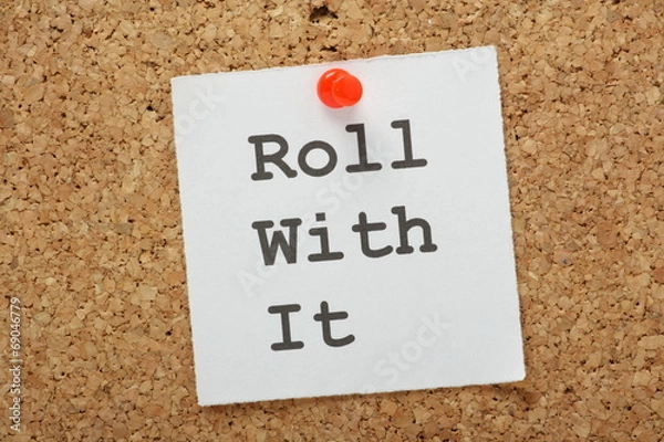 Fototapeta The phrase Roll With It on a cork notice board