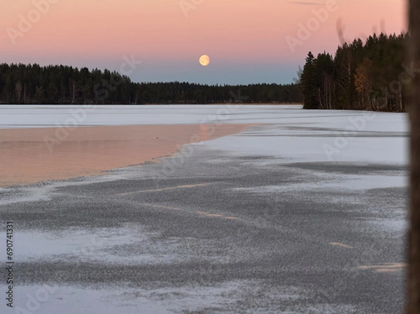 Fototapeta blue hour and moon rise on a lake in winter