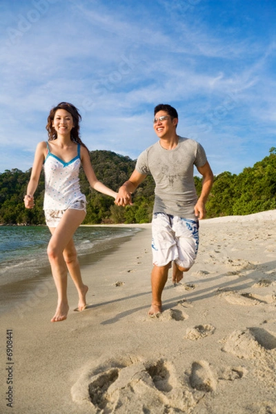 Fototapeta loving couple having fun running by the beach