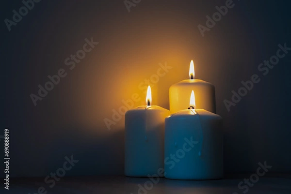 Fototapeta Three burning candles in the dark. Warm light from candles against cold dark background.