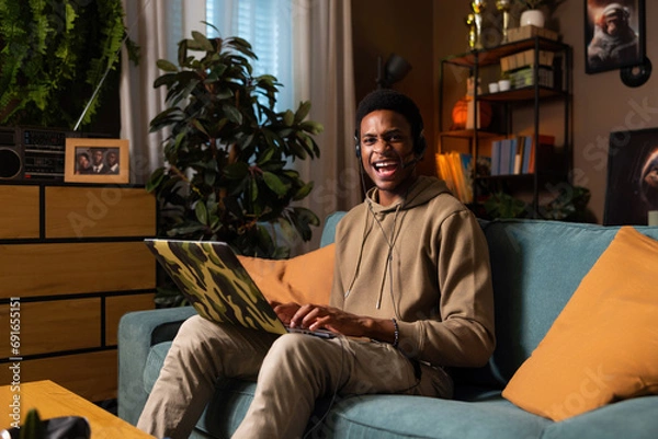 Fototapeta First job experience young guy student wearing wireless headset earphones working online in call center support hotline mature positive agent during conversation looking at camera.