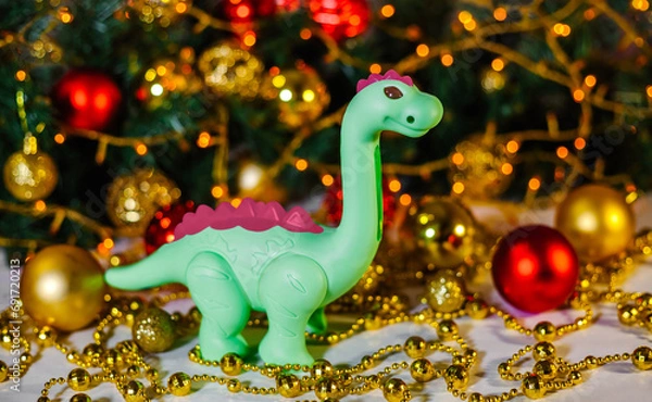 Fototapeta Green dragon on Christmas background. New Year's background of a Christmas tree and a golden garland. Dinosaur. Greeting card. Space for text. Chinese New Year. Christmas, New Year