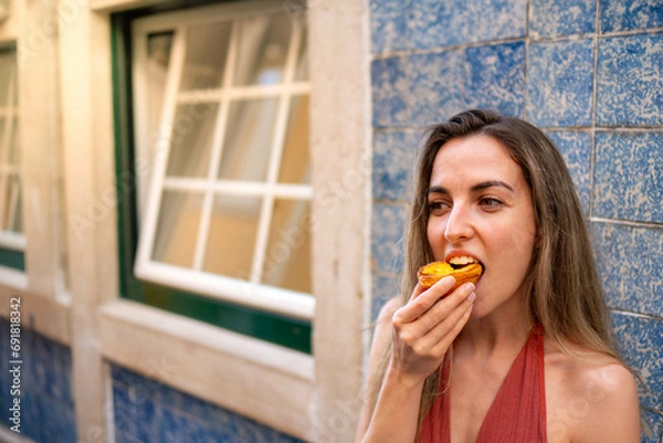 Fototapeta Close-Up, Frontal View of young Woman Enjoying a Traditional Portuguese Pastel de Nata, Captured Horizontally in Daylight