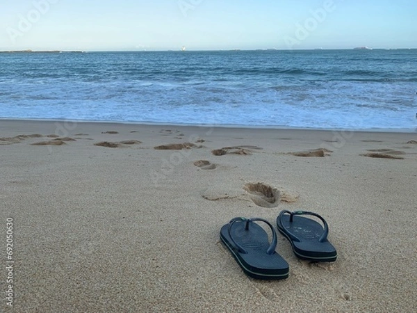 Fototapeta Vacation and relax. Flip flops alone on the beach in front of the blue ocean.