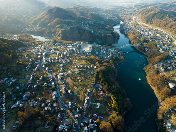 Fototapeta 夕日に照らされた紅葉した山々と田舎の町並み　空撮