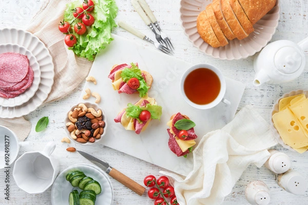Fototapeta Preparation sandwiches snack for morning meal or breakfast on white marble background. Sandwiches with slice salami, cheddar cheese lettuce and tomatoes cherry on white marble background. Top view.