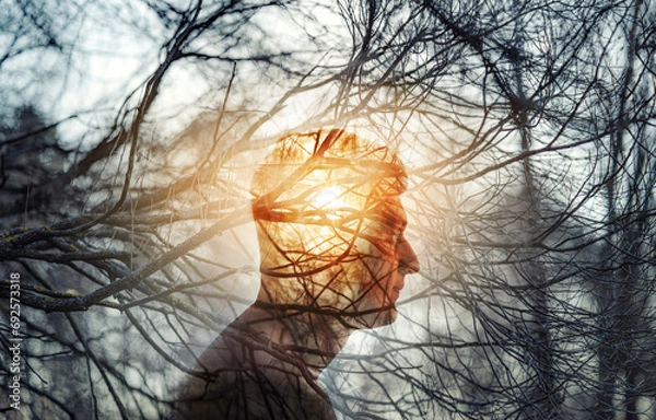 Obraz Head of a man on background of trees in forest. Topic of psychology, psychiatry, depression. The branches of trees symbolize problems and diseases, and the sun is a symbol of hope and recovery.
