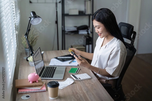Fototapeta Woman on desk with smartphone, credit card and ecommerce payment for online shopping at home. Happy female customer, digital bank app and sale on store website with internet banking