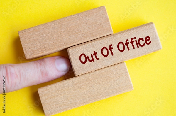 Fototapeta Finger pushing out wooden block with out of office text on yellow cover background