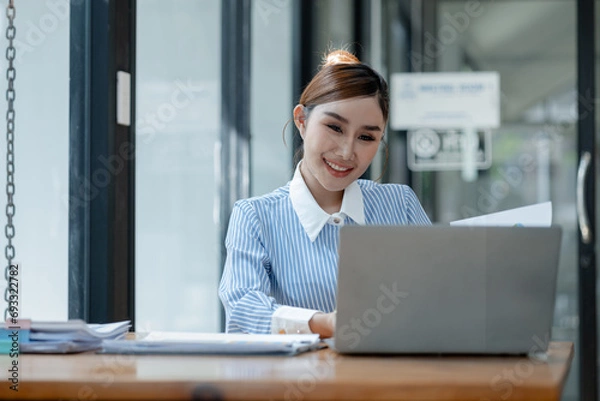 Fototapeta Businesswoman is sitting and working in the office, Employee is looking for information on laptop, Recording various information on paper, Employees sit and take notes in the office.