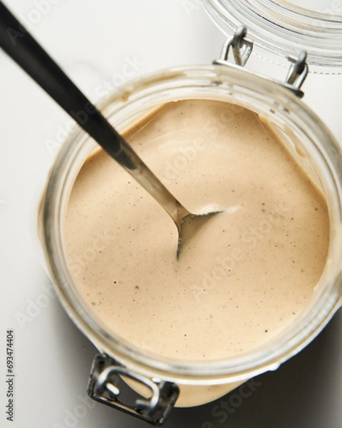 Fototapeta Tarator - Lebanese sauce from tahini with garlic, lemon juice and water. White or cream colored sauce in a jar on a marble background