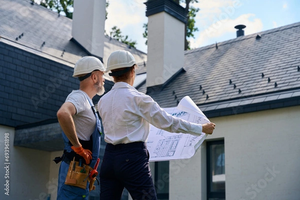 Fototapeta Builder and site supervisor conducting cottage facade inspection