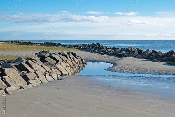 Fototapeta Beach with erosion-control rip-rap and small tidal pool in the foreground and Atlantic Ocean in the background.
