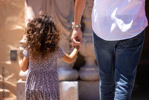 Obraz Child holding parents hand while walking outside.
